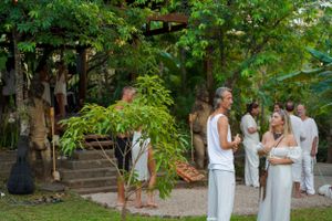 People in white clothing mingling at an outdoor garden party surrounded by lush greenery.