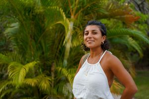 Woman in white dress smiling confidently against tropical palm background.