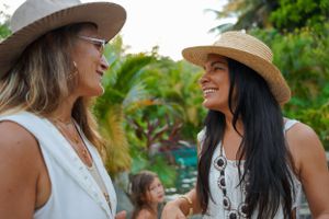 Two people in straw hats sharing a joyful moment outdoors with tropical foliage in the background.