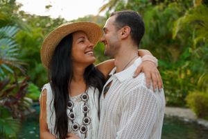 A couple in white outfits sharing an intimate moment in a lush tropical garden setting.