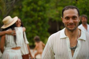 Person in white knit sweater smiling while standing in a garden with others in background.