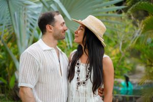 Couple in white outfits sharing a romantic moment against tropical palm trees.
