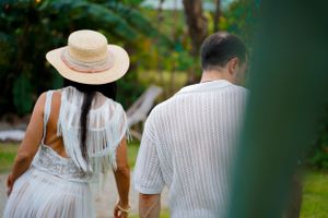 Couple in white attire walking through a tropical garden pathway.