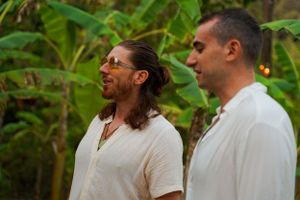 Two guests in light-colored clothing converse against a backdrop of tropical plants.