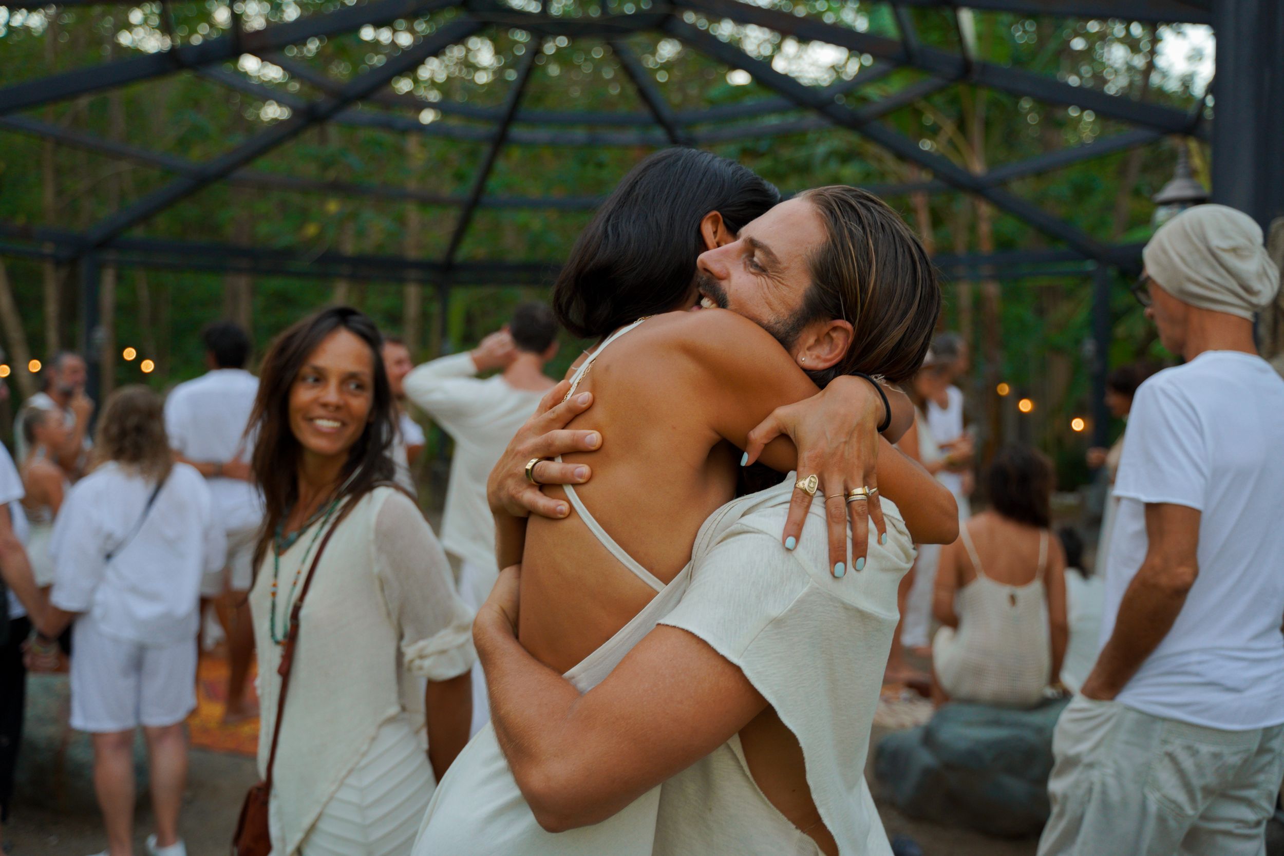 Guests share warm embraces at an all-white outdoor celebration.