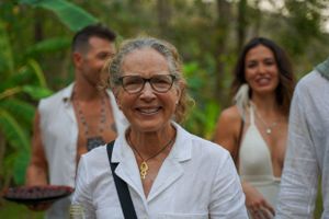 A festive outdoor gathering with guests in white attire surrounded by tropical greenery.