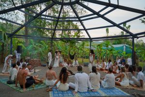People gather on blankets under a glass-ceiling structure for an outdoor event surrounded by greenery.