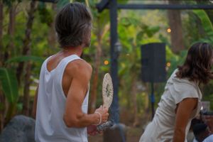 Dancing outdoors under string lights at a garden gathering while holding a traditional drum.