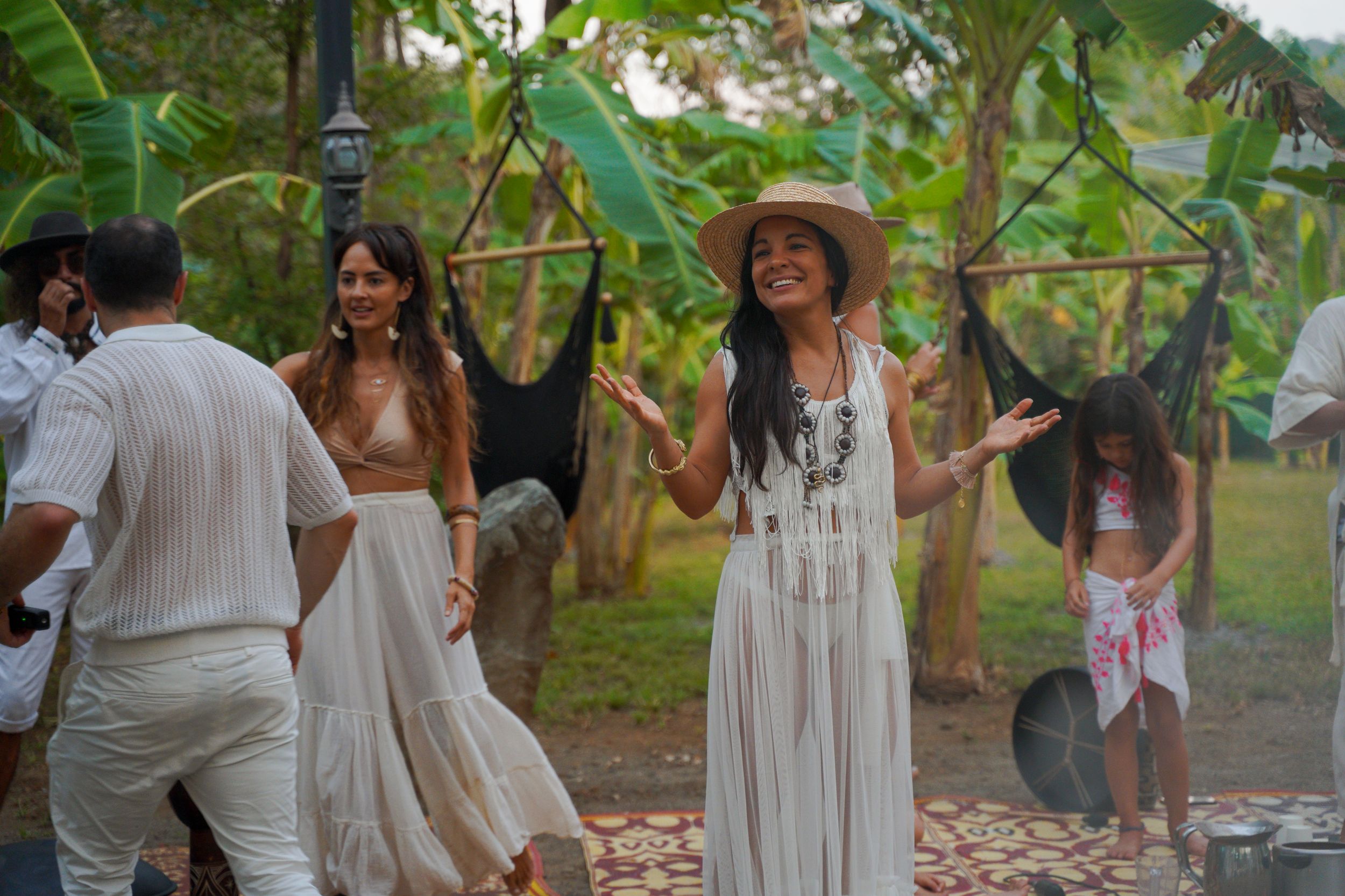 Dancers in flowing white dresses move gracefully in a tropical garden setting.
