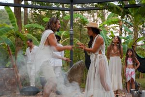 People participate in a ceremonial gathering with smoke and traditional elements in an outdoor setting.