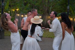 People in white clothing celebrate together under string lights in a garden setting.
