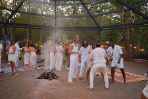 A group gathered around a fire pit wearing all white clothing at an outdoor event.