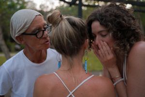 Three people huddled together sharing secrets and laughing outdoors.