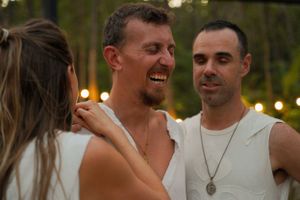 Three people sharing a joyful moment together at an outdoor evening gathering.