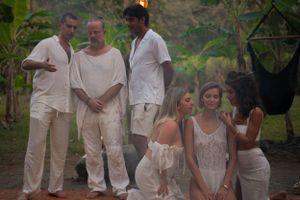 People in white clothing gather for a social event in a tropical garden setting.