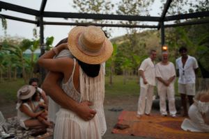 Couple embracing under a garden pergola with others in the background.