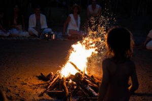 Silhouette of person watching sparks fly from large bonfire in darkness.