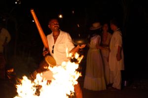 Fire performer wielding flaming torch in white clothing during nighttime ceremony.