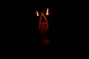 Dramatic dark photo of a mysterious glowing red figure with raised arms in darkness.