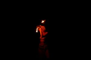 Eerie red-lit silhouette performing in dark space with flame effect.