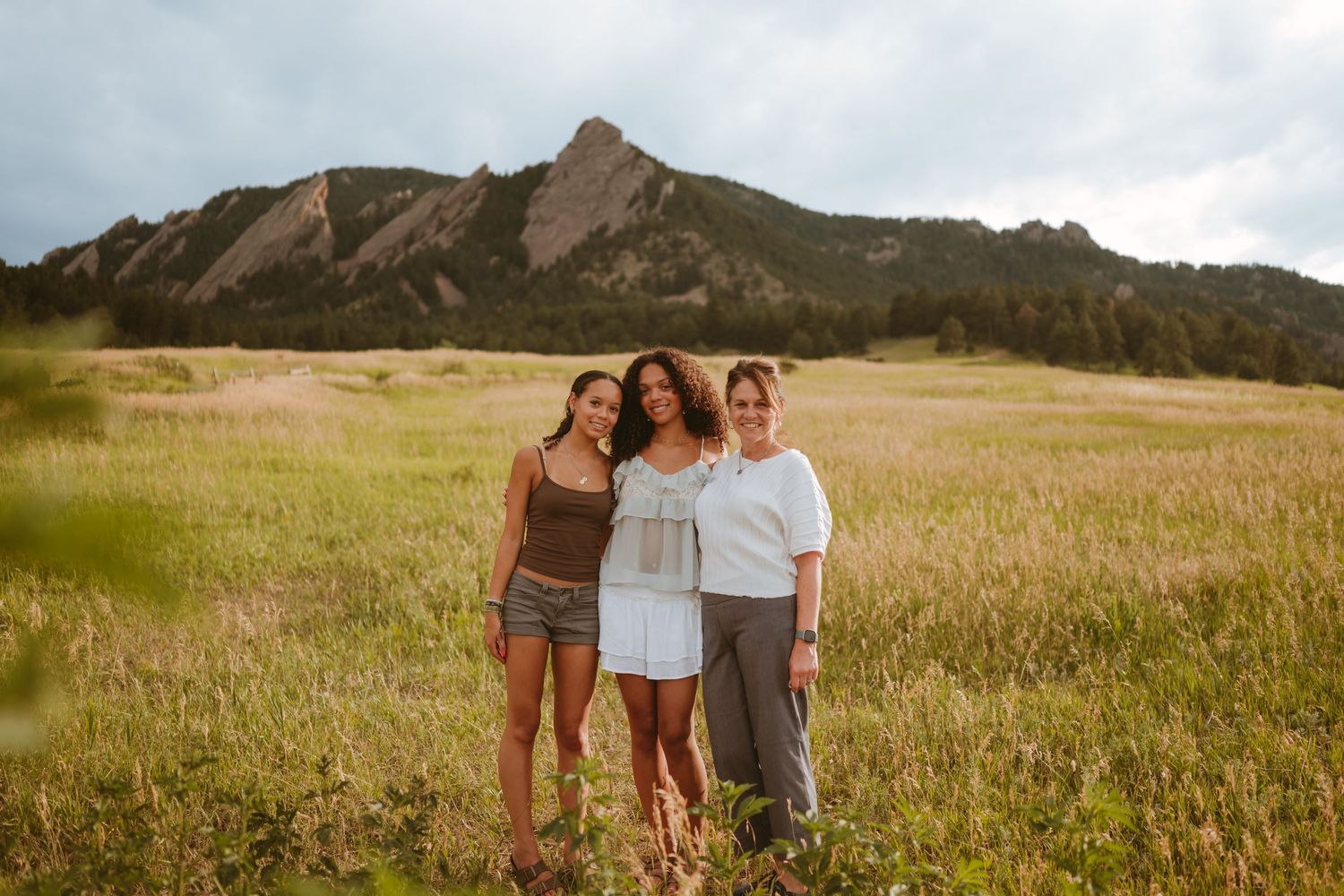 A family shares a joyful moment in a golden meadow with majestic Flatiron mountains rising in the background.