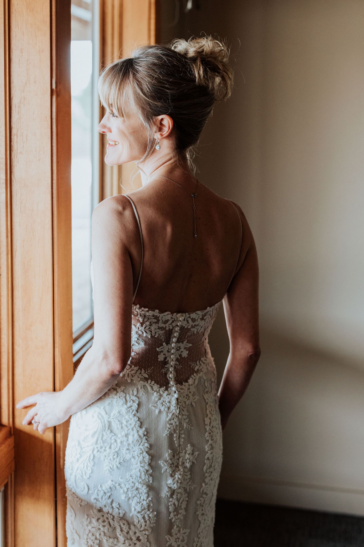Woman in a lace wedding dress looking out a window.