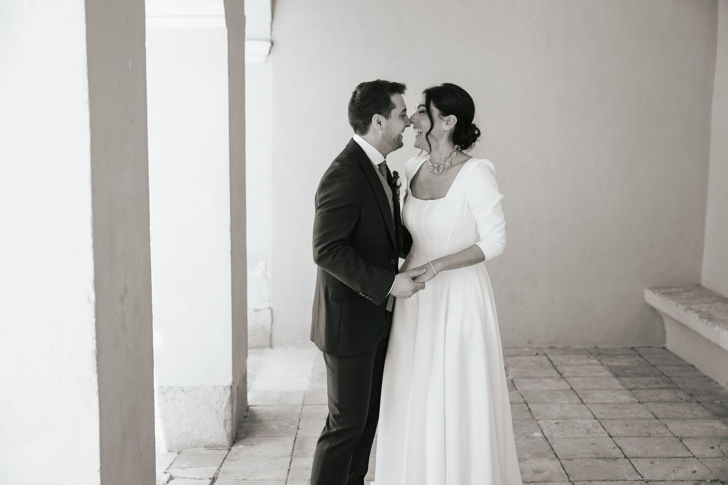 Fotografía en blanco y negro de una pareja de novios besándose durante el día de su boda.
