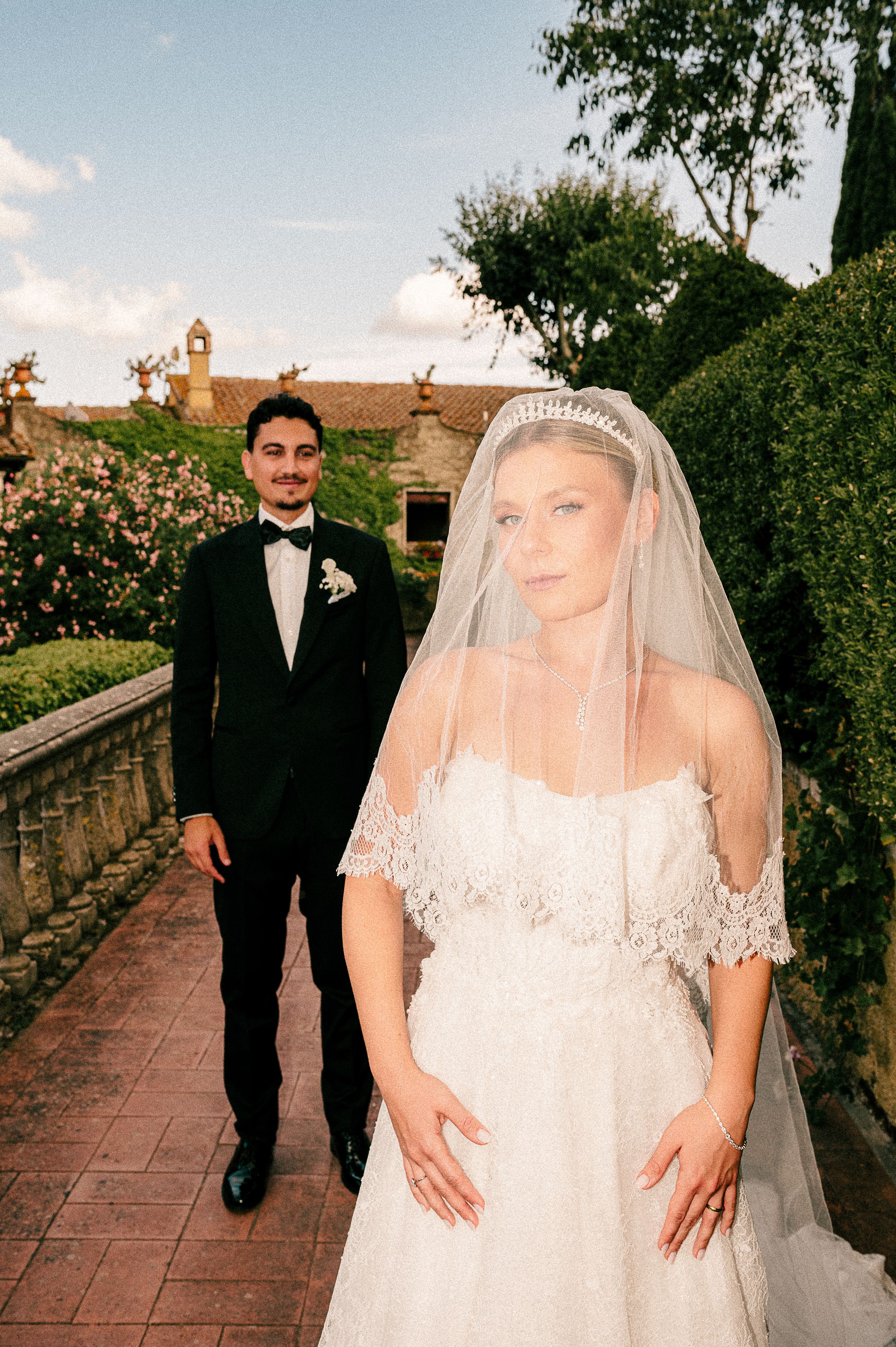 A wedding couple poses along a Mediterranean villa's stone pathway at golden hour.