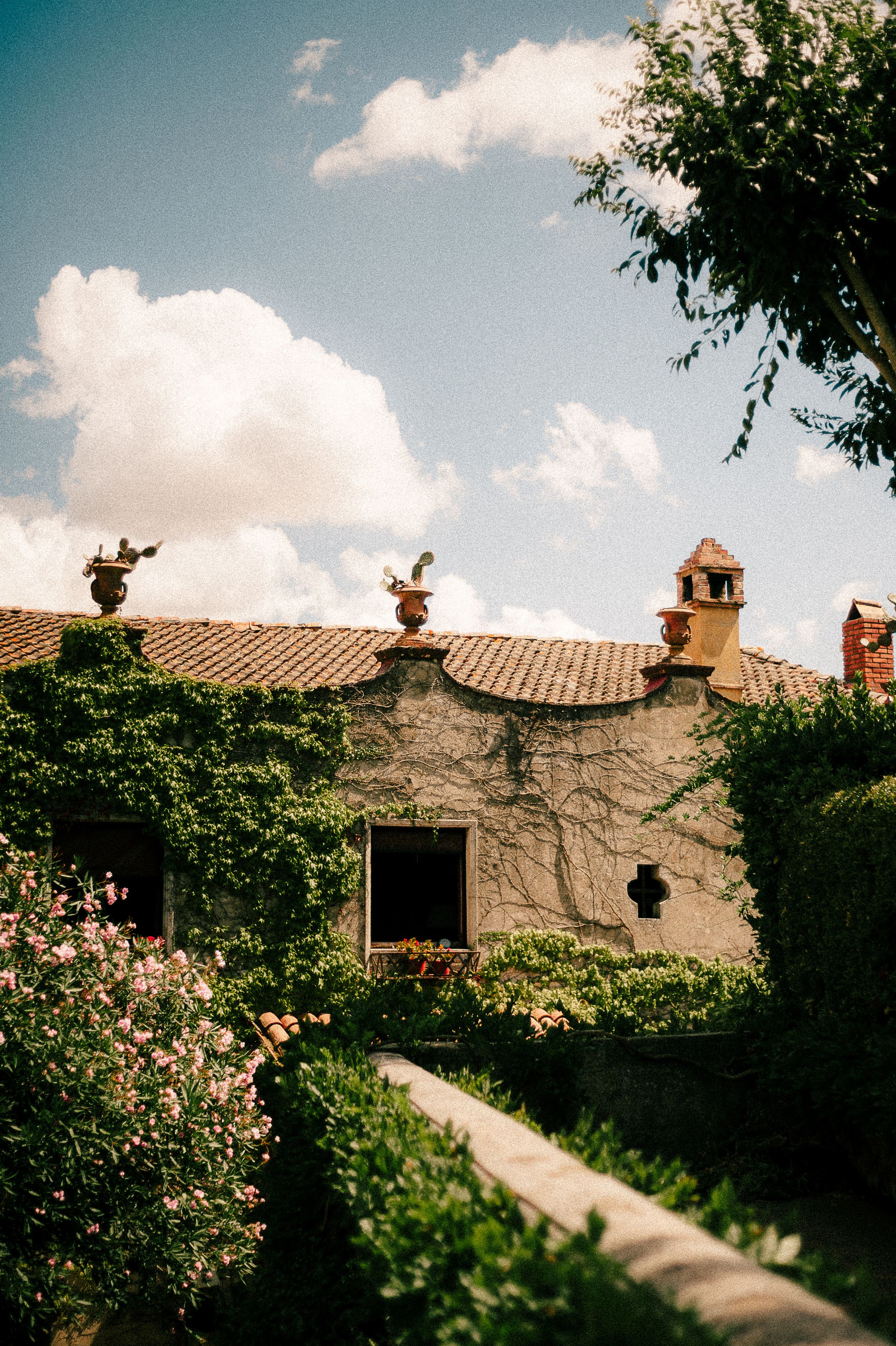 A rustic Mediterranean villa with terracotta roof tiles and ornate finials against a blue summer sky with puffy clouds.