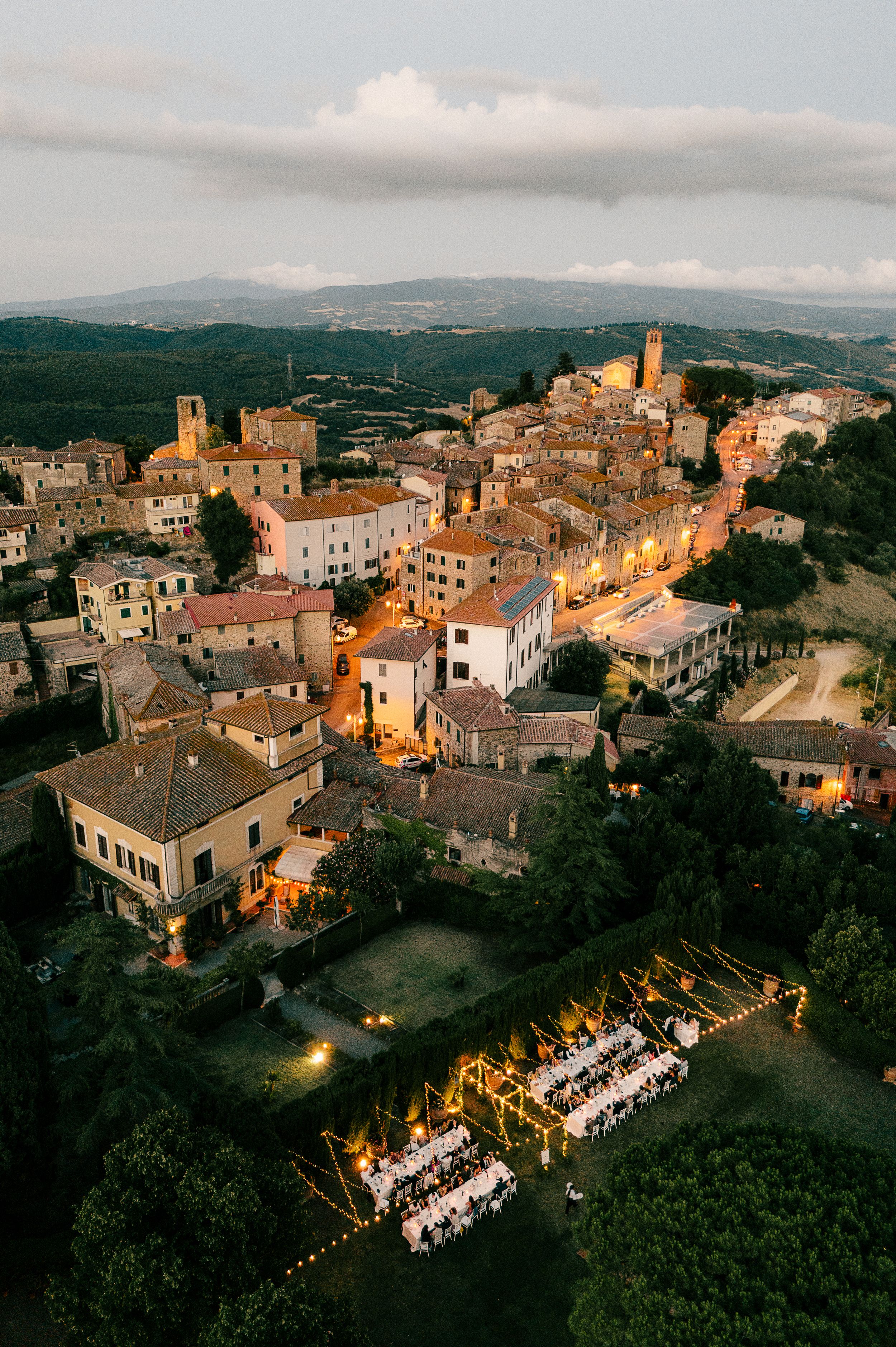 Aerial view of a rustic Italian village with long dinner tables set up for an outdoor wedding reception.