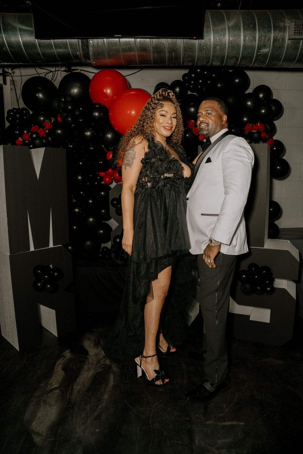 A couple dips and dances together at a celebration with black and red balloons decorating the dark space.