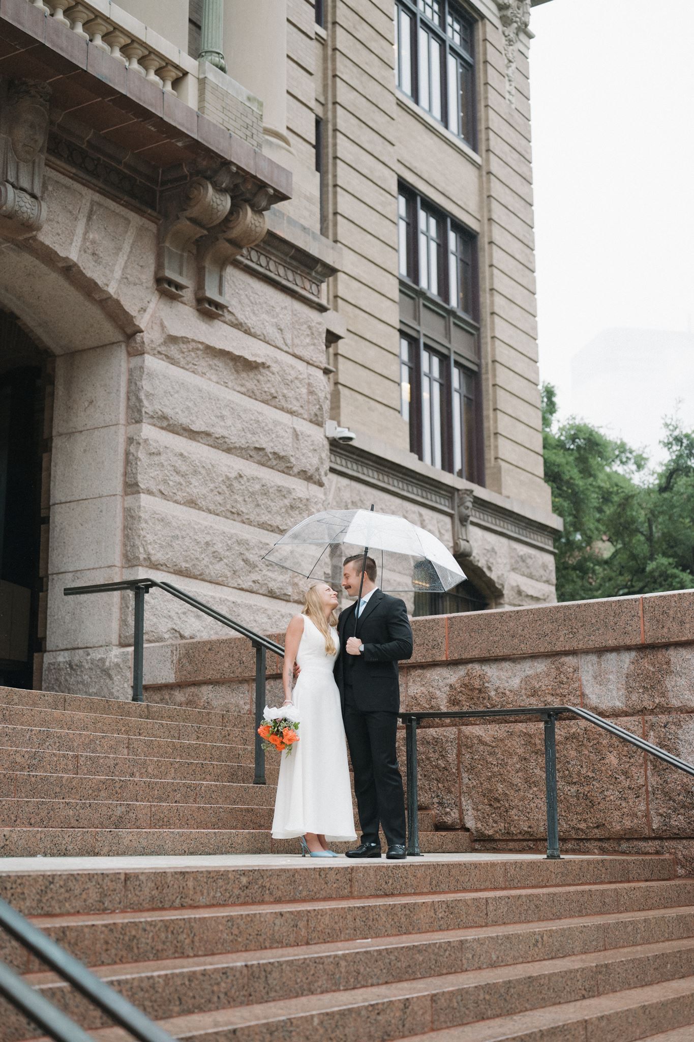Bride and groom snuggled together under an umbrella at 1910 Courthouse in Houston, Tx.