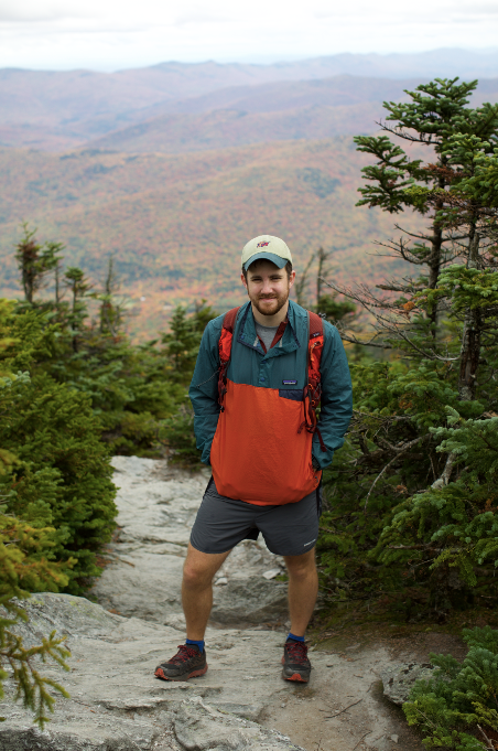 A hiker poses on rocky terrain with sweeping mountain views in autumn colors.
