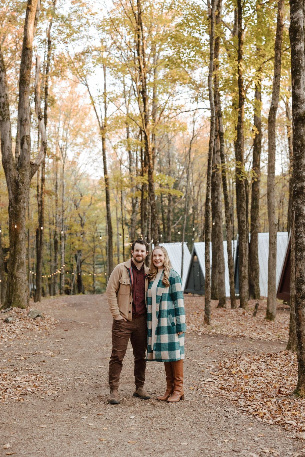 A couple walking through a scenic autumn forest with fallen leaves covering the ground.
