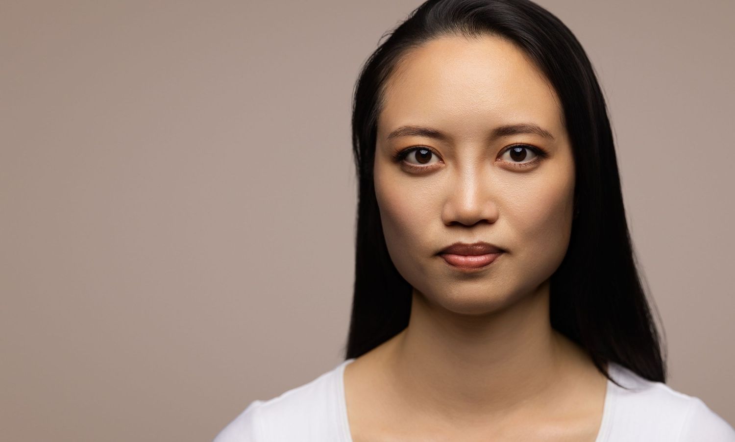 Professional portrait in neutral tones featuring an East Asian woman wearing a white top against a brown background.