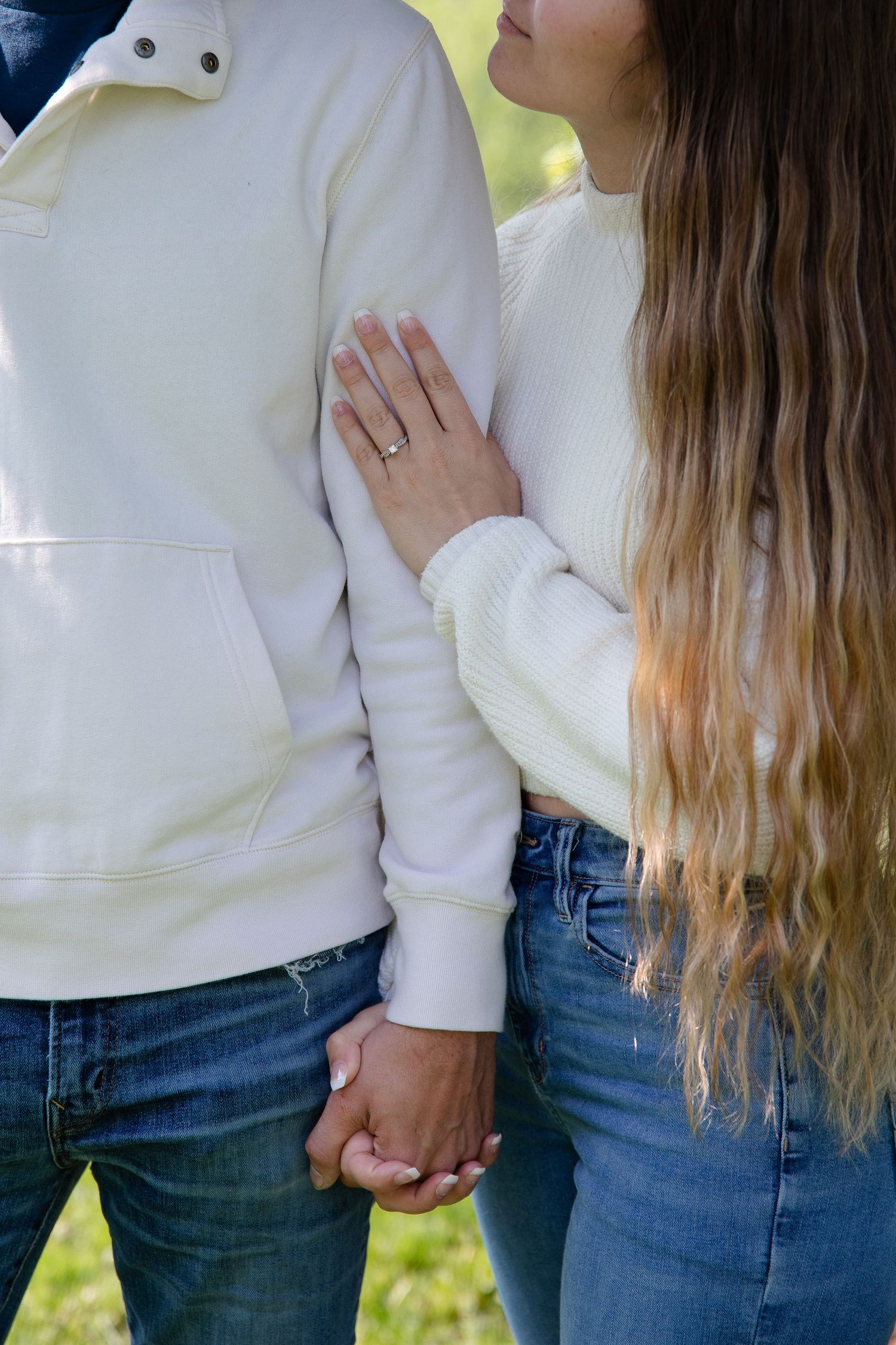 Two people in matching white sweaters and jeans embracing outdoors. Couples photo session. Engagement photo session