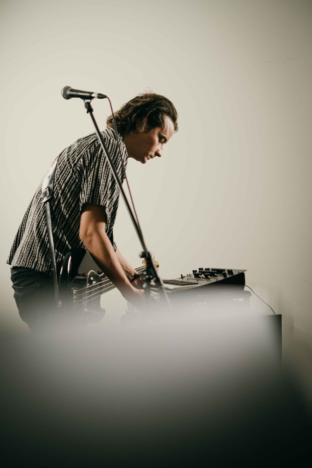 Musician in striped shirt performing with electronic equipment against white wall.