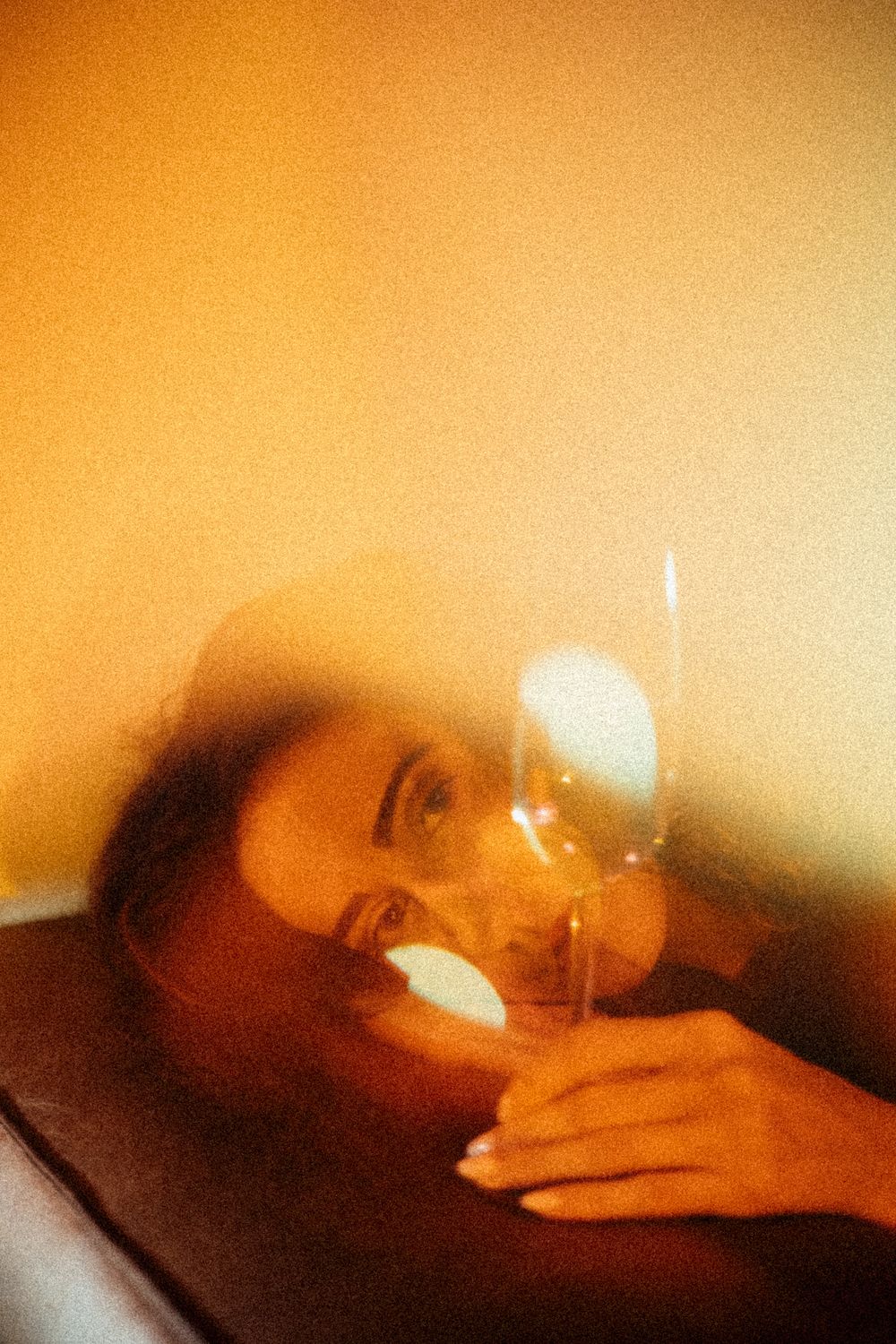 Woman reclining with wine glass in warm golden light, dreamy film photography aesthetic.