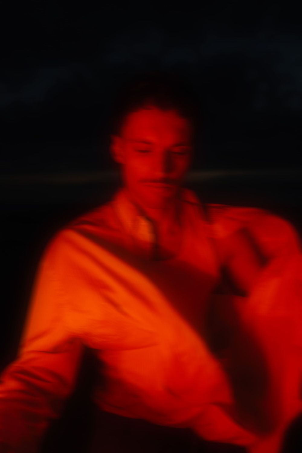 Blurry artistic portrait of a person bathed in dramatic red light against a dark background.