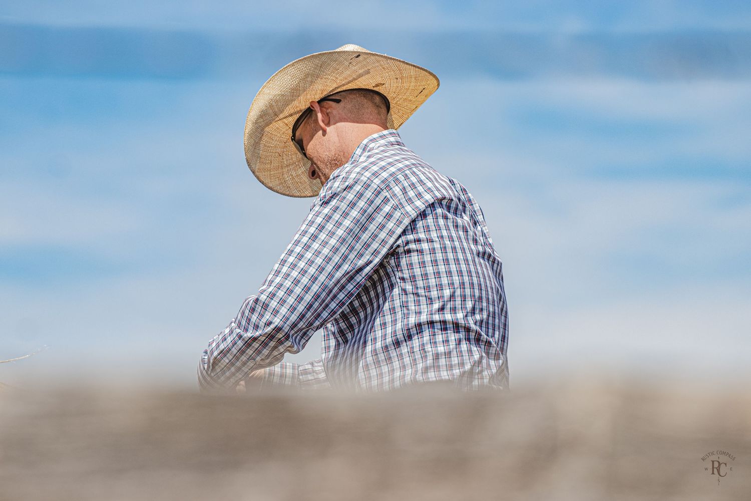 Cowboy behind a rustic wooden fence in a straw cowboy hat with a beautiful blue sky background