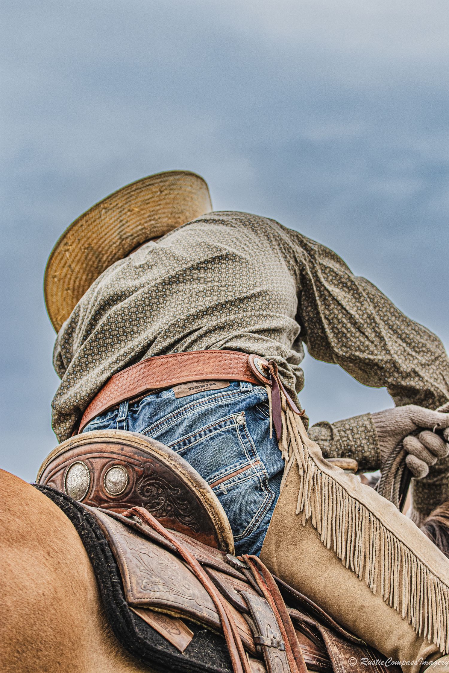 Cowboy leaning over his saddle sorting out his rope during a branding with a beautiful blue sky background