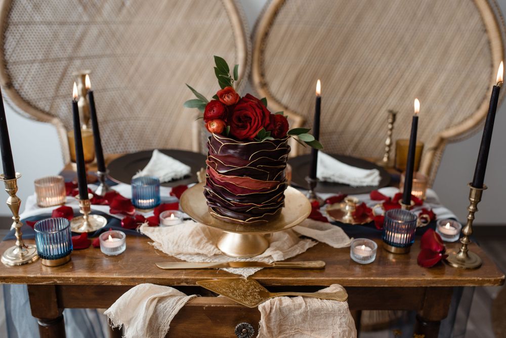 Elegant wedding table setting with dark cake, red roses, and gold candle holders.