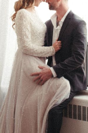Intimate wedding portrait showing details of lace dress and formal attire in soft window light.