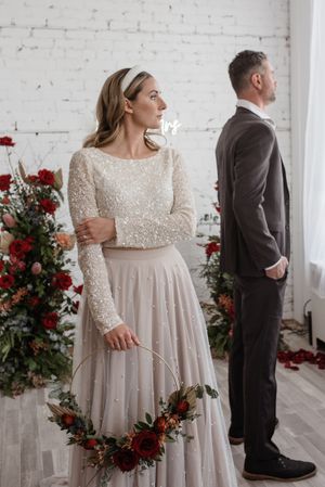 Wedding couple posed separately with red floral arrangements in a white brick interior.