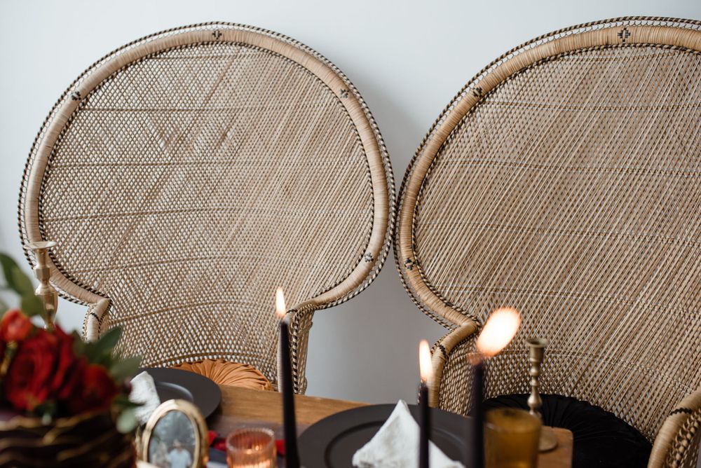 Elegant rattan peacock chairs with lit candles and floral decorations for wedding reception.