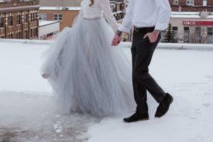 Lower half view of couple walking in snow, bride wearing flowing grey tulle gown.