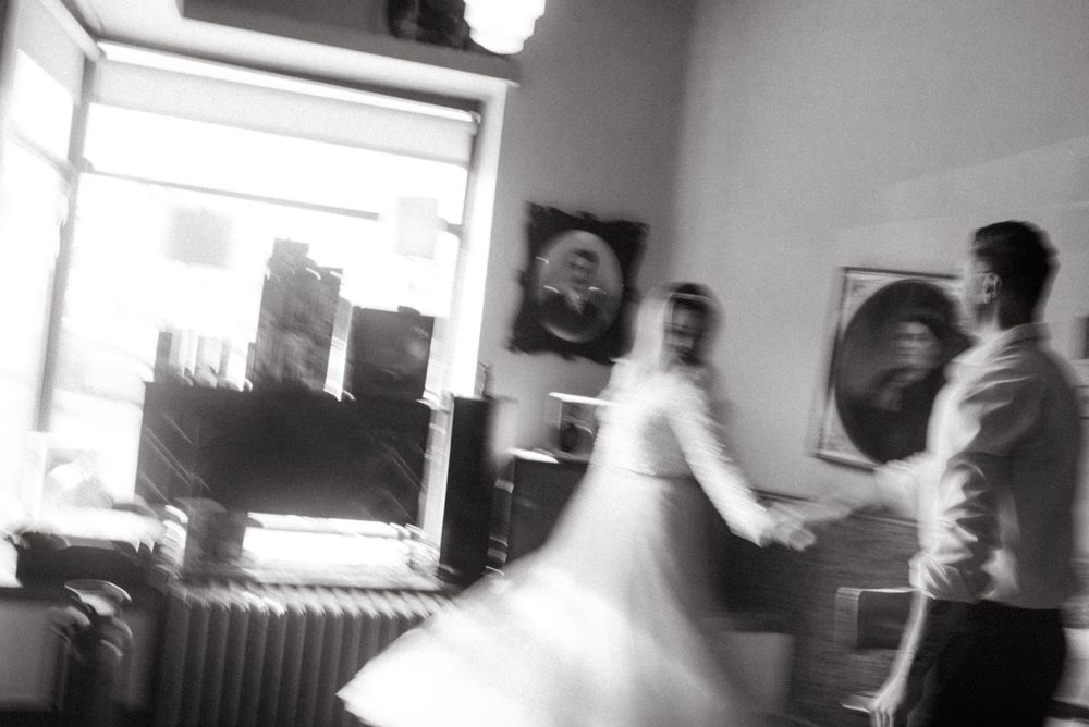 A blurred black and white motion shot of two people dancing in a room with portraits on the wall.