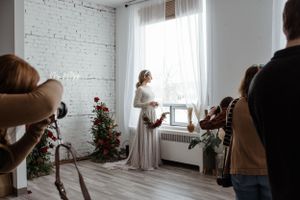 Behind-the-scenes of bridal photoshoot in bright studio with white brick walls and floral decorations.