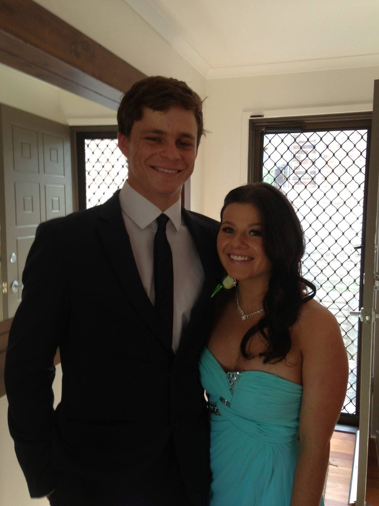 Young couple in formal attire poses together, with woman in turquoise dress and man in dark suit.