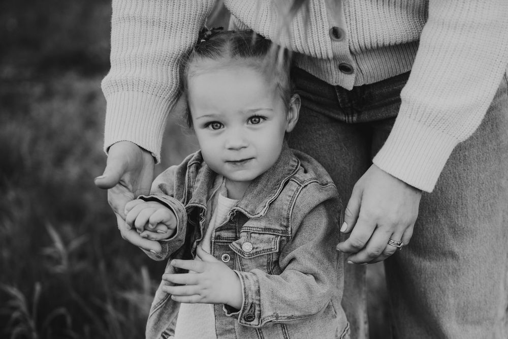 A small toddler in a floral dress stands close to an adult wearing light colored clothing in a black and white photo.